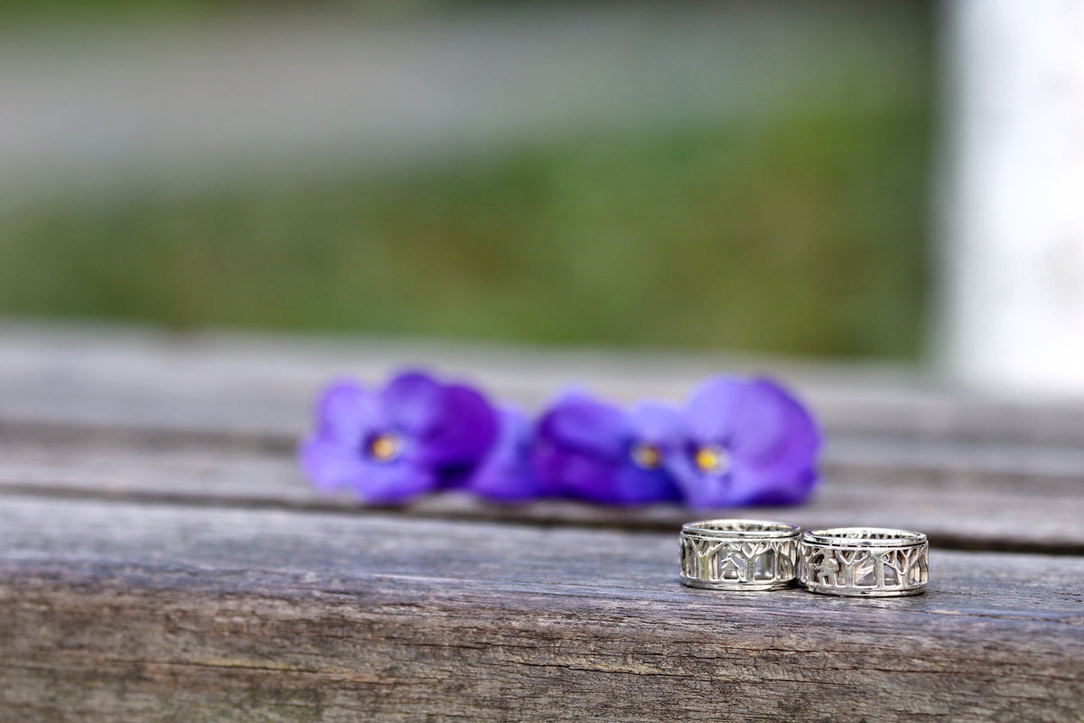 Two sterling silver spinner rings with an openwork tree design on weathered wood, purple violets behind