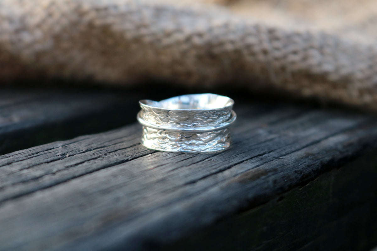 Simplicity sterling silver spinner ring with a textured band on weathered wood