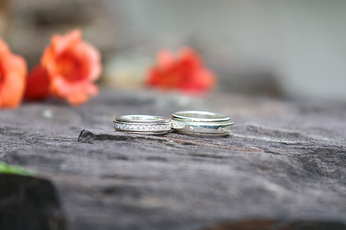 Two sterling silver spinner rings side by side on weathered stone, red blossoms behind