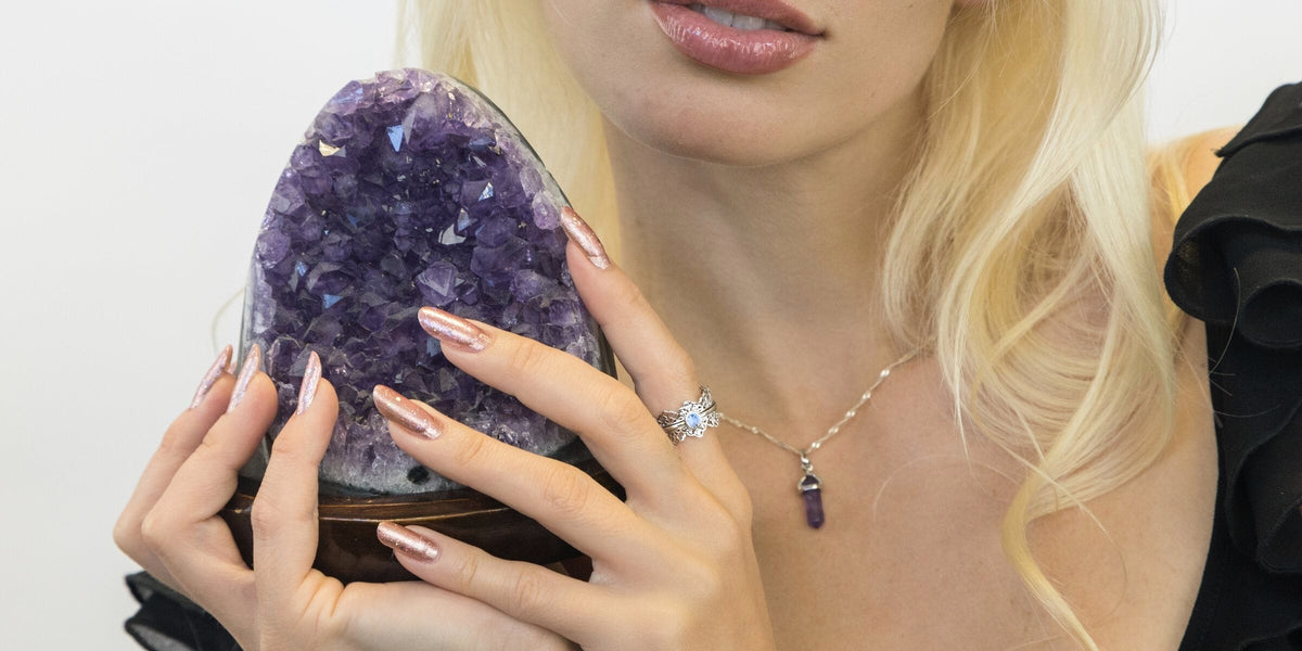 Model holding an amethyst geode, wearing a filigree spinner ring with a light sapphire