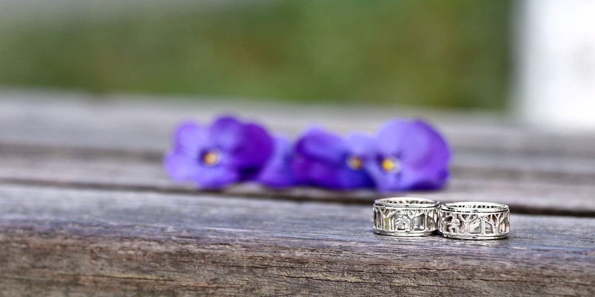 Two silver spinner rings with a forest cutout on a wooden table beside violets
